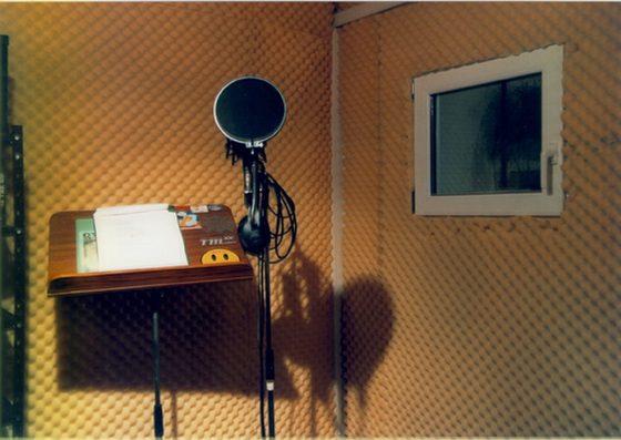 Die Gesangskabine. Mikrofon mit Popschutz, Notenpult, Schallschutz an der Wand, daneben das Sichtfenster zur Regie.